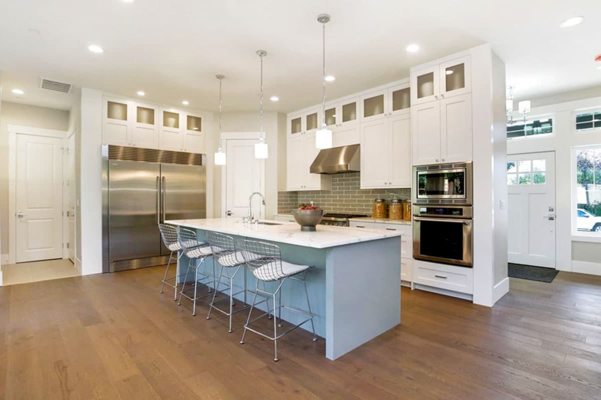 Contemporary kitchen with large island, stainless steel appliances, white cabinetry, and hardwood floors.