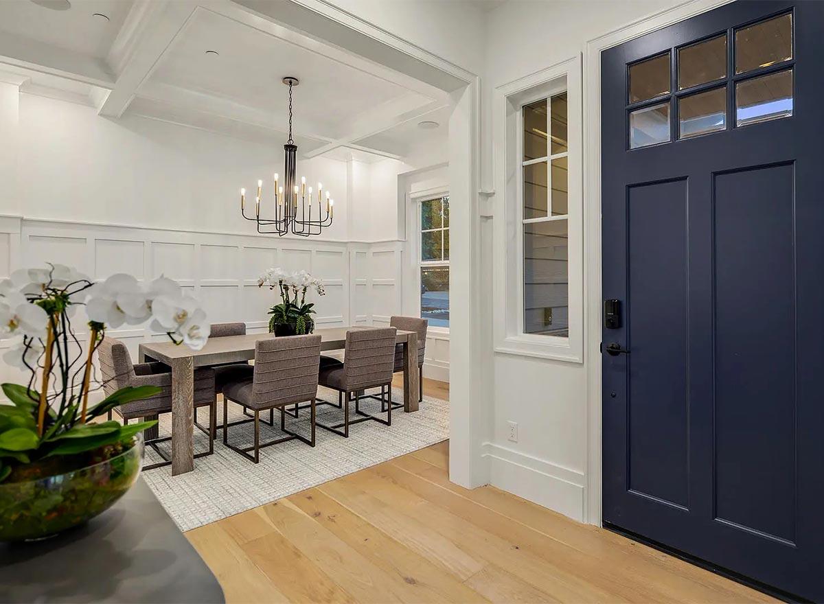 Interior view of a dining room with coffered ceiling, wainscoting, chandelier, and a navy front door.