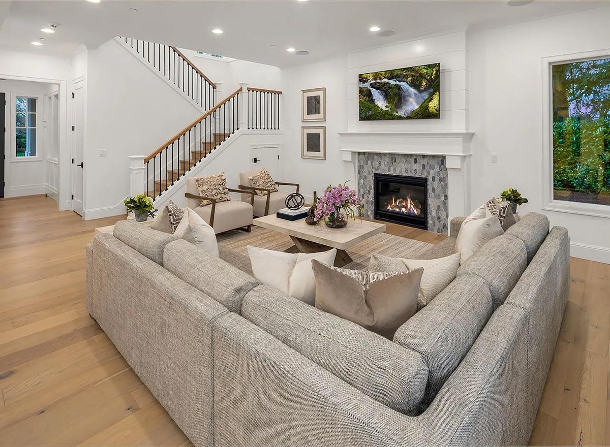 Great room with sectional sofa, fireplace with hexagonal tile surround, wood floors, and staircase with black spindles.