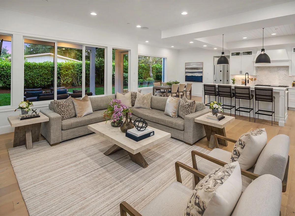 Open concept living area with large windows, sectional sofa, coffee table, and kitchen island with bar stools.