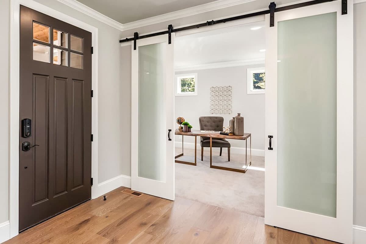 Interior view of entryway with dark paneled door and frosted sliding barn door leading to office with desk and chair.