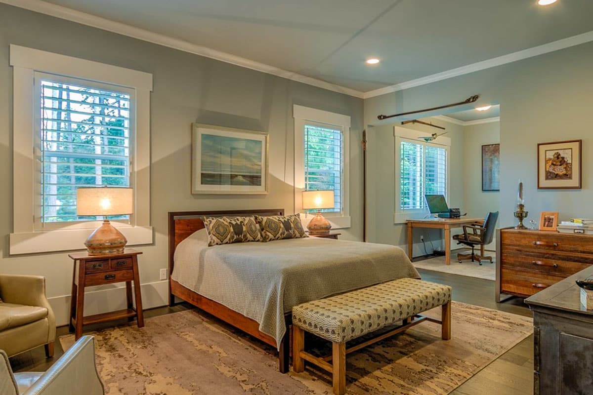 Interior view of a bedroom with a bed, bench, and adjacent workspace featuring a desk and chair.
