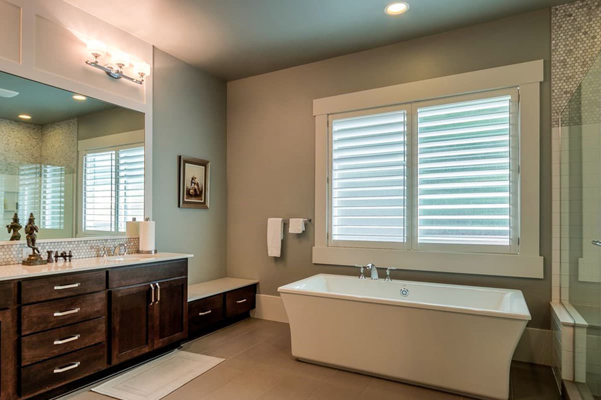 Bathroom with freestanding tub, dark wood vanity with double sinks, and louvered windows.