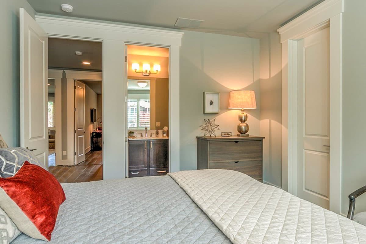 Bedroom with view into ensuite bathroom. Features a dresser with lamp and doorway to hallway.