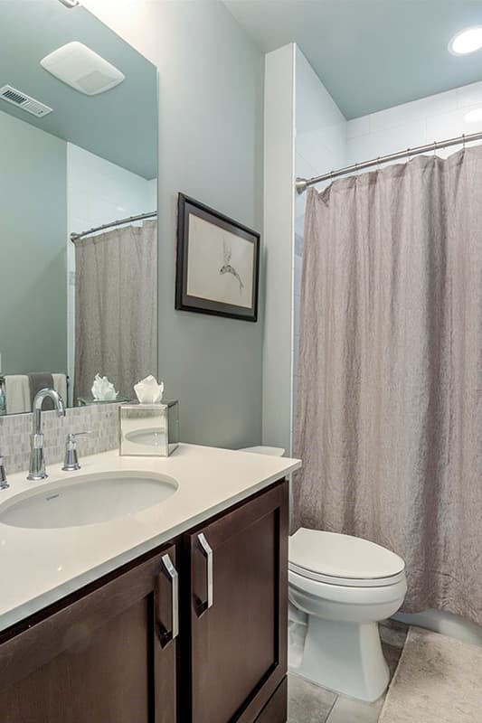Bathroom interior with vanity, toilet, and shower with gray curtain. Features mosaic tile backsplash and framed art.