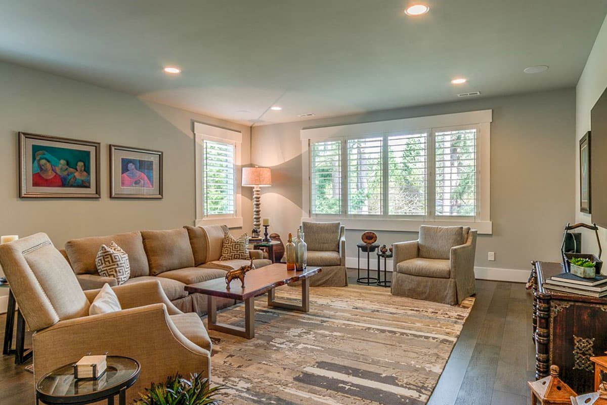 Living room with sectional sofa, two armchairs, live-edge coffee table, large patterned rug, and plantation shutters on windows.