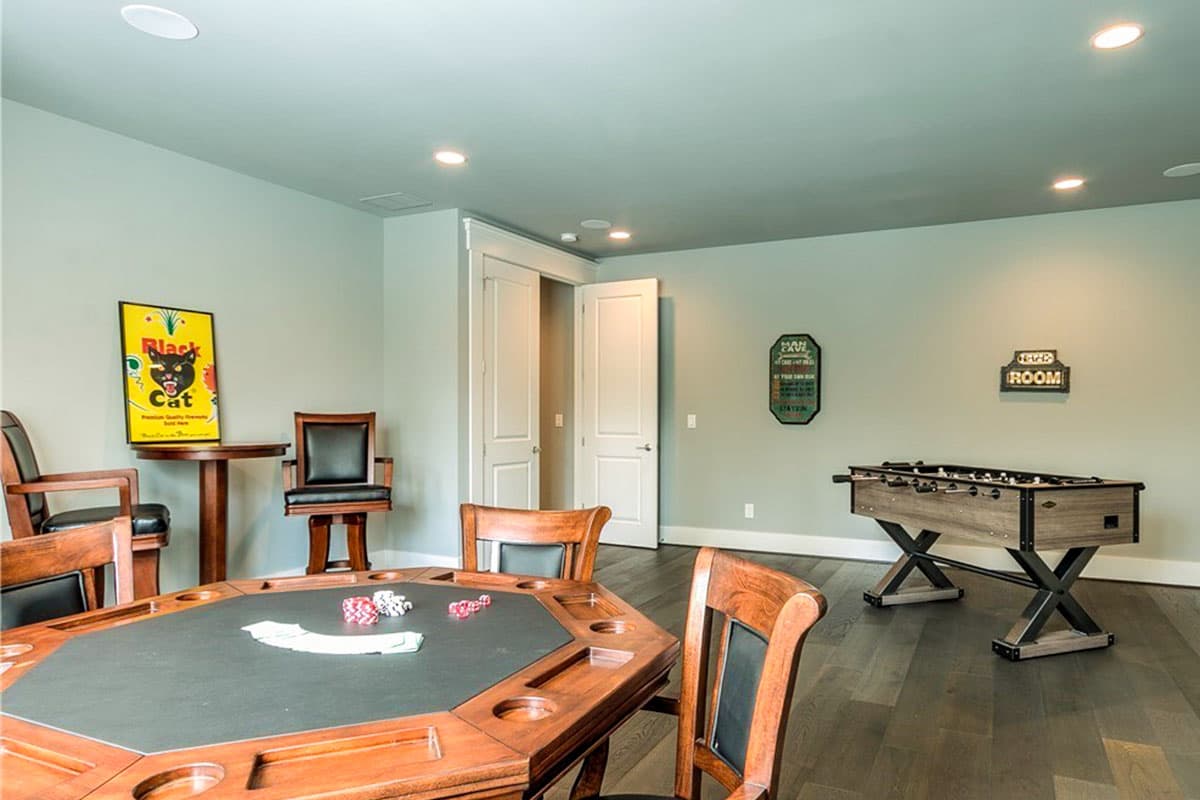 Recreation room interior with poker table, foosball table, and two chairs against a light green wall.