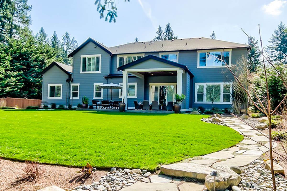 Two-story house plan exterior with covered patio, multi-pane windows, and gabled rooflines.