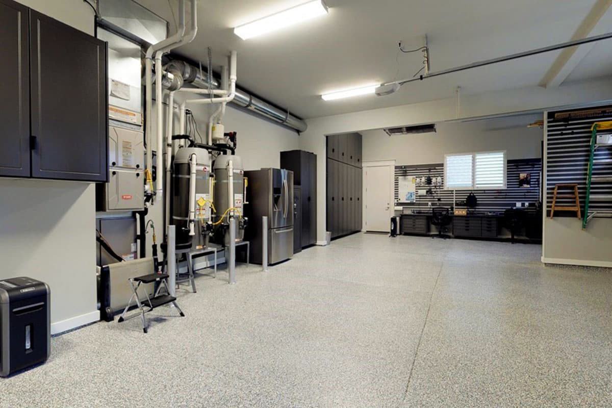 Garage interior with HVAC units, refrigerator, storage cabinets, workbench, and pegboard wall organization.