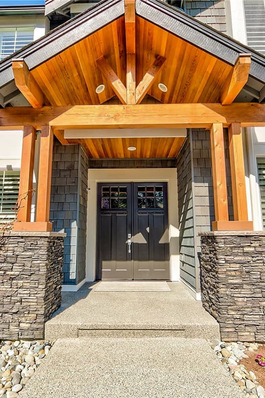 House plan exterior: Modern entryway with double doors, stone pilasters, wood beams, and decorative gables.