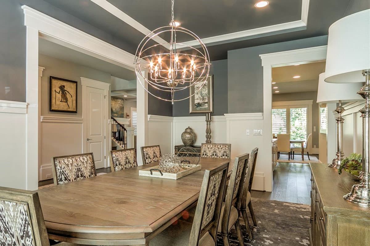 Dining room with coffered ceiling, wooden table, upholstered chairs, and view into hallway with staircase.