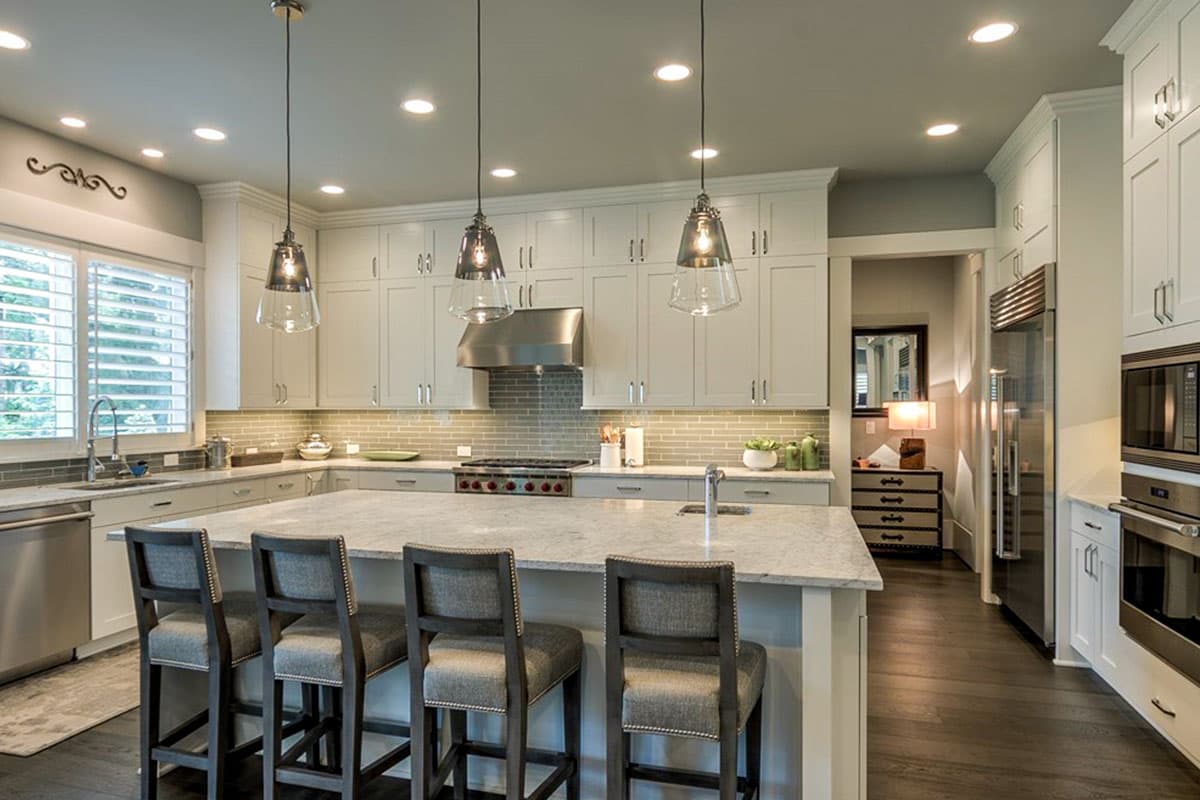 Kitchen with island, pendant lights, white cabinetry, stainless steel appliances, and subway tile backsplash.