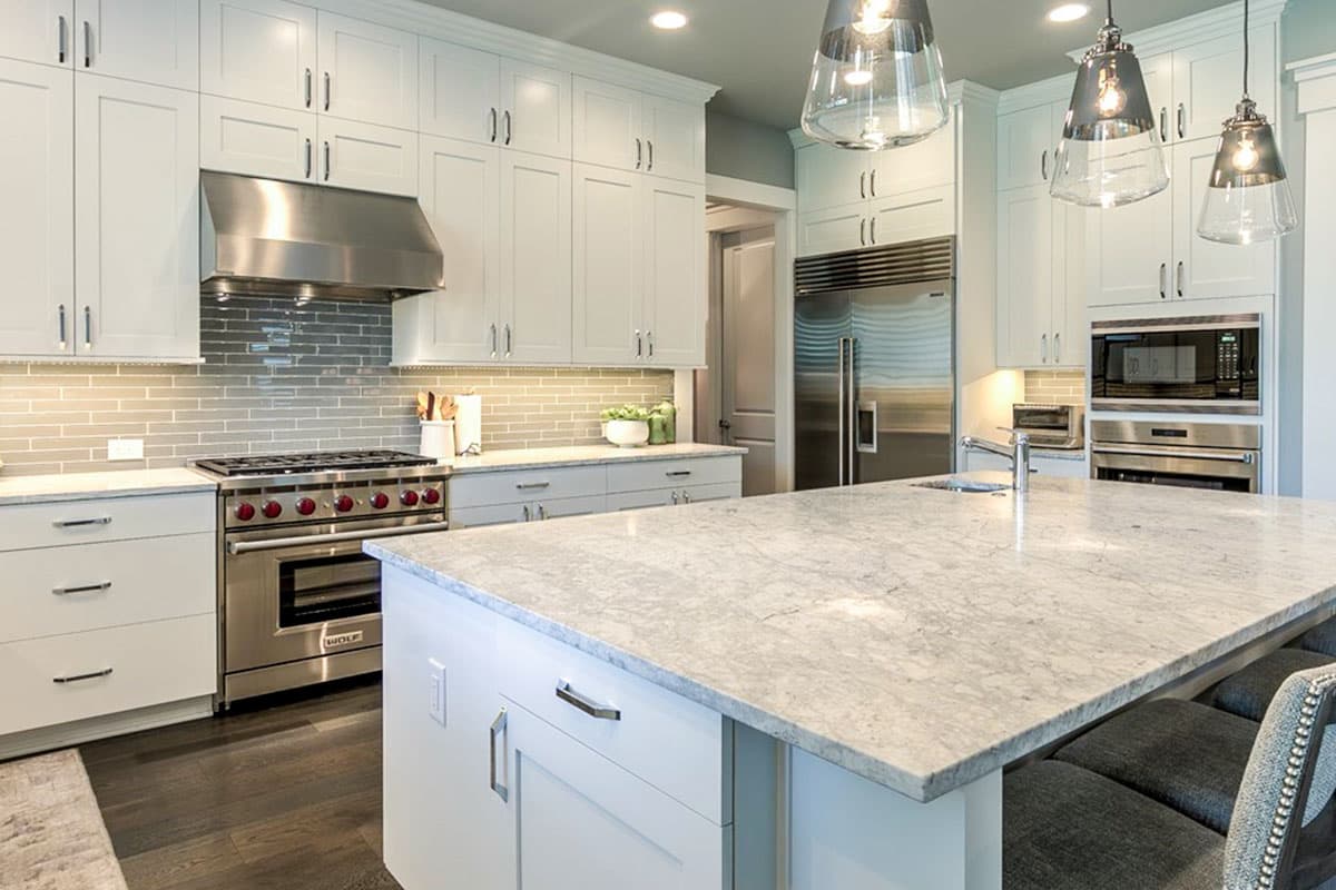 Kitchen interior with white cabinets, gray subway tile backsplash, stainless steel range, and large island with granite countertop.