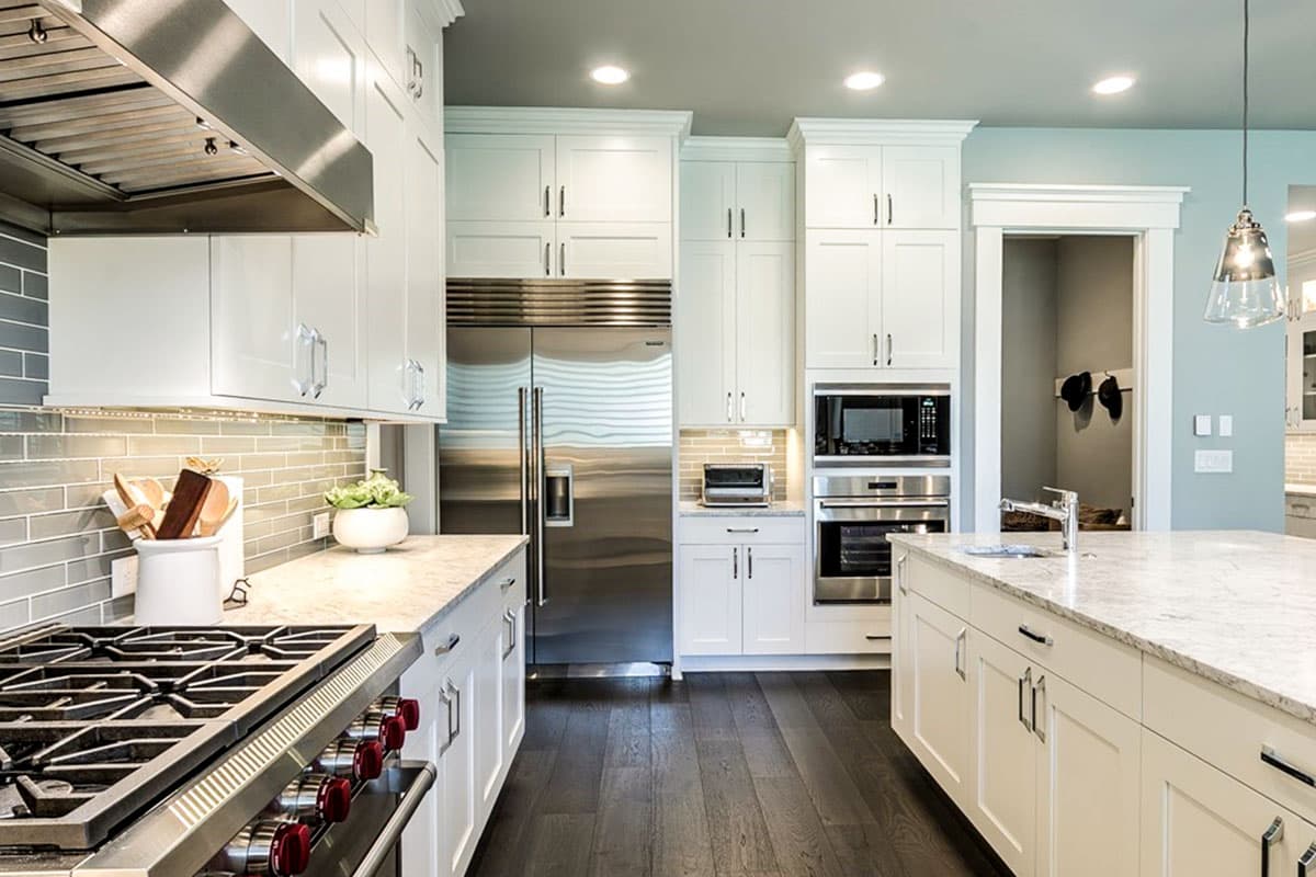 Kitchen with white cabinetry, stainless steel appliances including a Sub-Zero refrigerator, gas range, and island.
