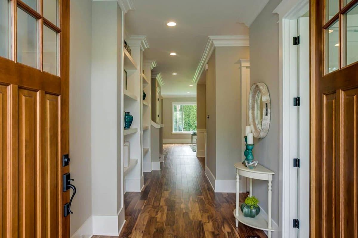 Interior view of a hallway with hardwood floors, built-in shelving, and natural light from a window at the end.