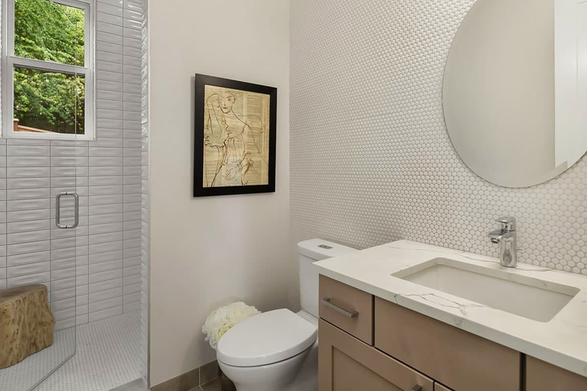Powder room with tiled shower, toilet, vanity with sink, and modern artwork.
