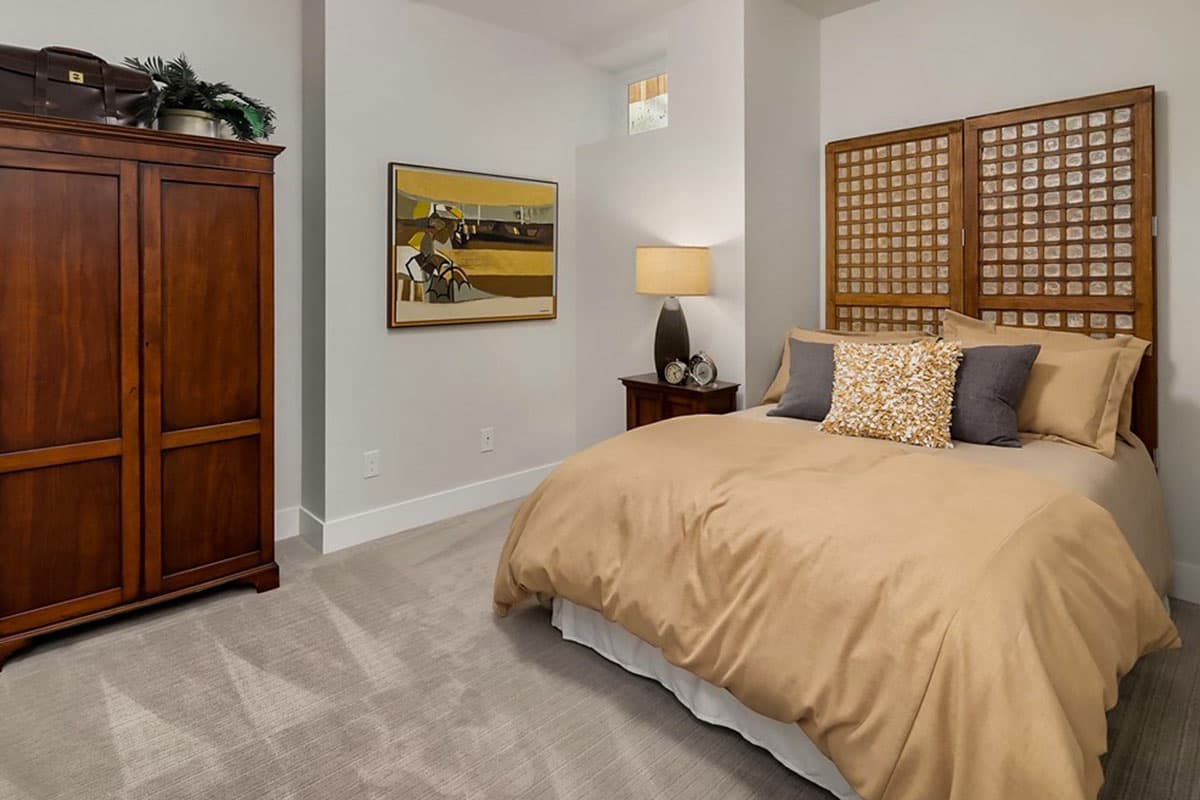 Bedroom with queen bed, wooden armoire, bedside table with lamp, and abstract artwork.