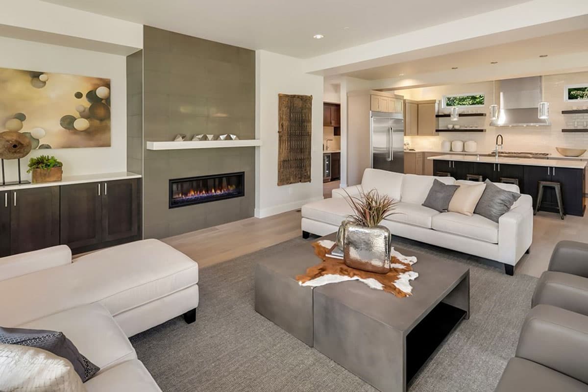 Modern living room with linear fireplace, sectional sofa, and open-concept kitchen with island and stainless steel appliances.
