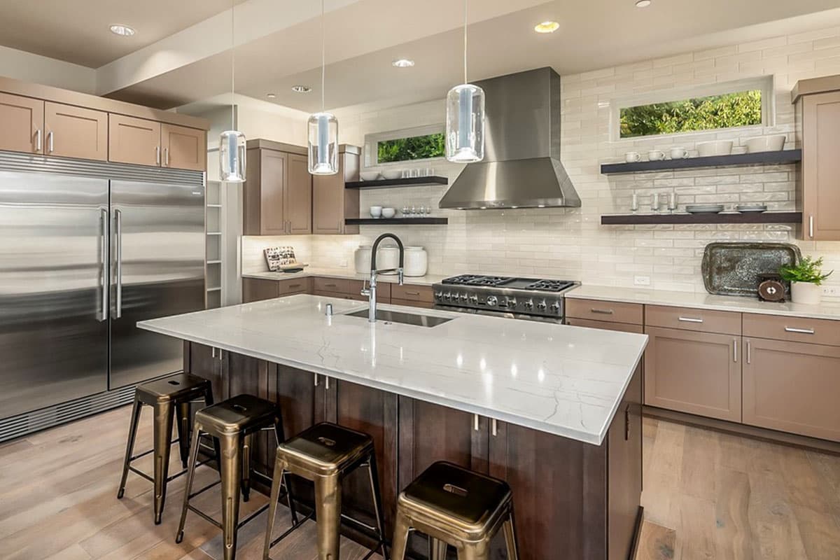 Kitchen with island, stainless steel appliances, gas range, range hood, subway tile backsplash, and pendant lighting.