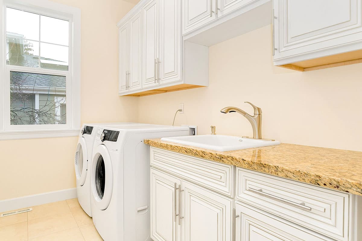 Laundry room with white cabinetry, granite countertop, sink, faucet, washer, and dryer, with a window view.
