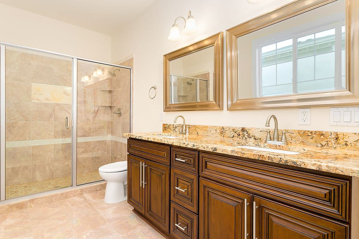 Bathroom features glass-enclosed tiled shower, dual vanity with granite countertop, wood cabinetry, and large mirrors.