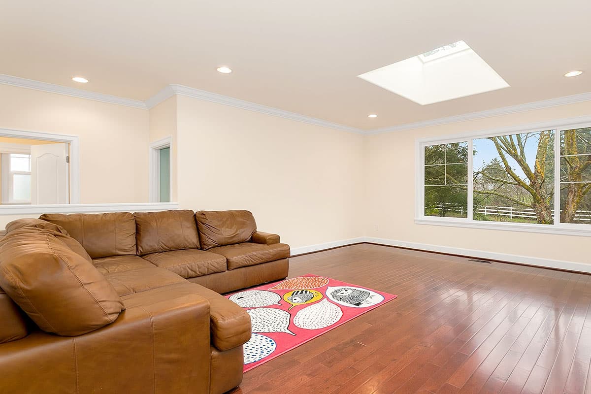 Living room with leather sectional sofa, skylight, large picture window, and hardwood floors.