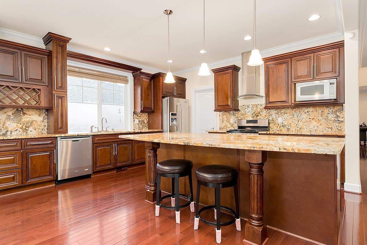 Kitchen with dark wood cabinets, granite countertops, large island with seating, stainless steel appliances, and hardwood floors.