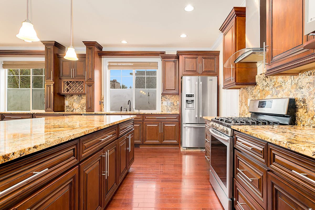 Interior kitchen view showing dark wood cabinetry, granite countertops, stainless steel appliances, and a central island.