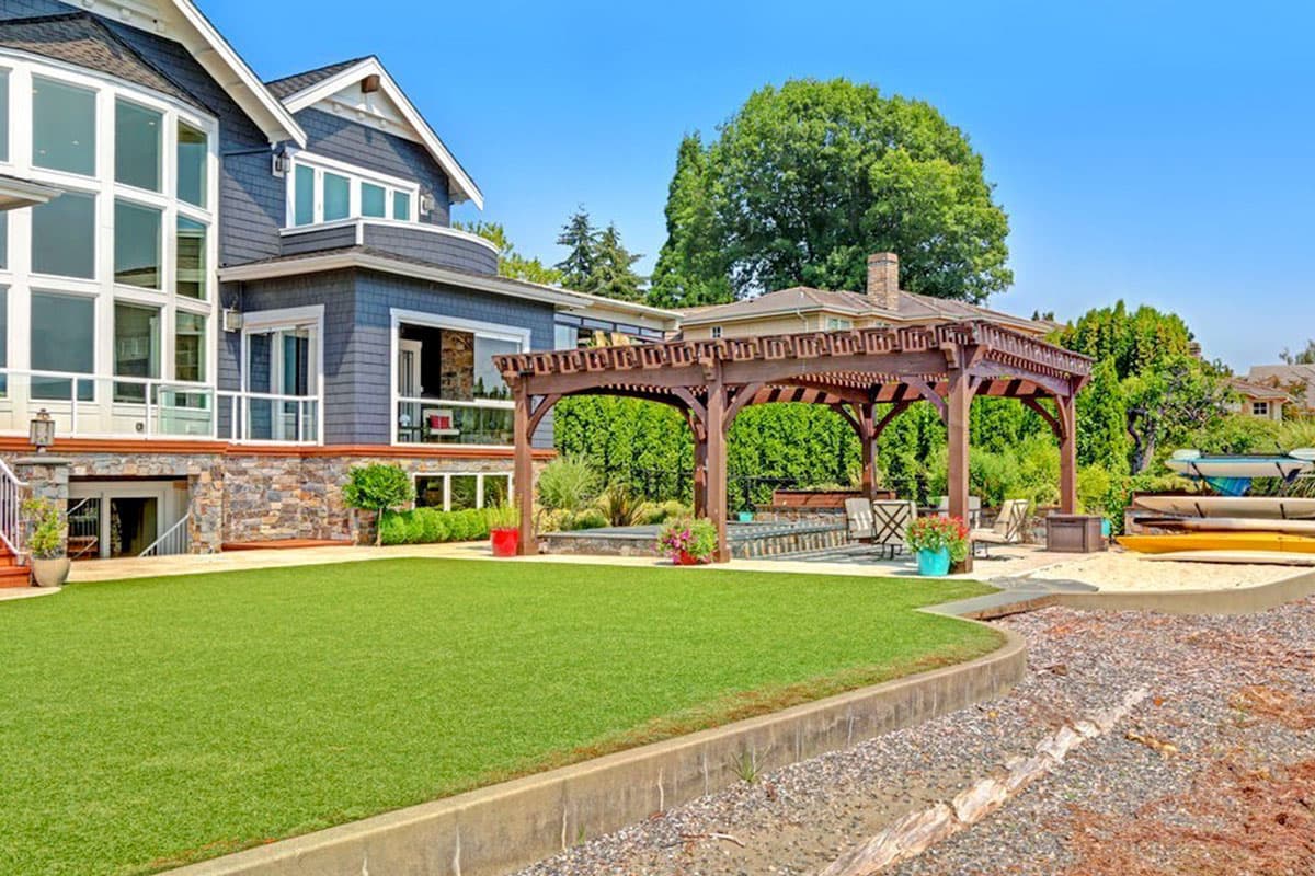 House plan exterior showing a multi-story home with large windows, stone accents, and a wooden pergola over a patio.