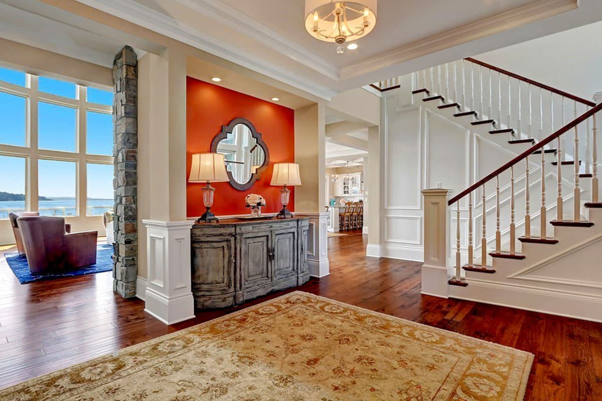Interior view of foyer with stone column, large windows, decorative console table, and staircase with white balusters.