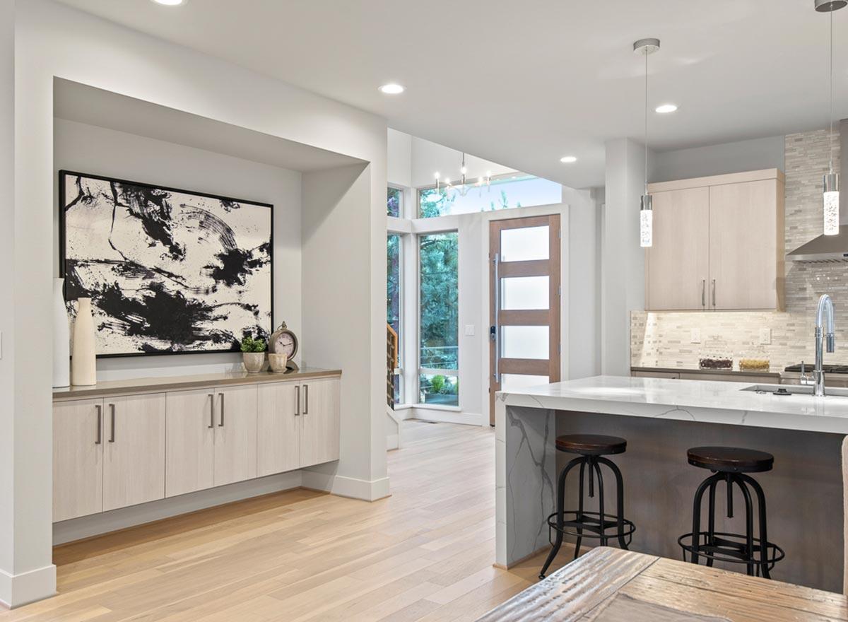 Interior view of a modern kitchen and entryway with a waterfall island, linear cabinets, and a wood-paneled door.