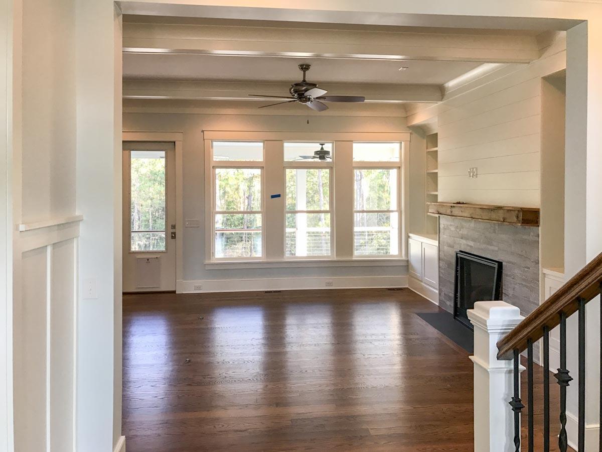Interior view of a great room with coffered ceiling, fireplace, built-in shelving, and large windows.