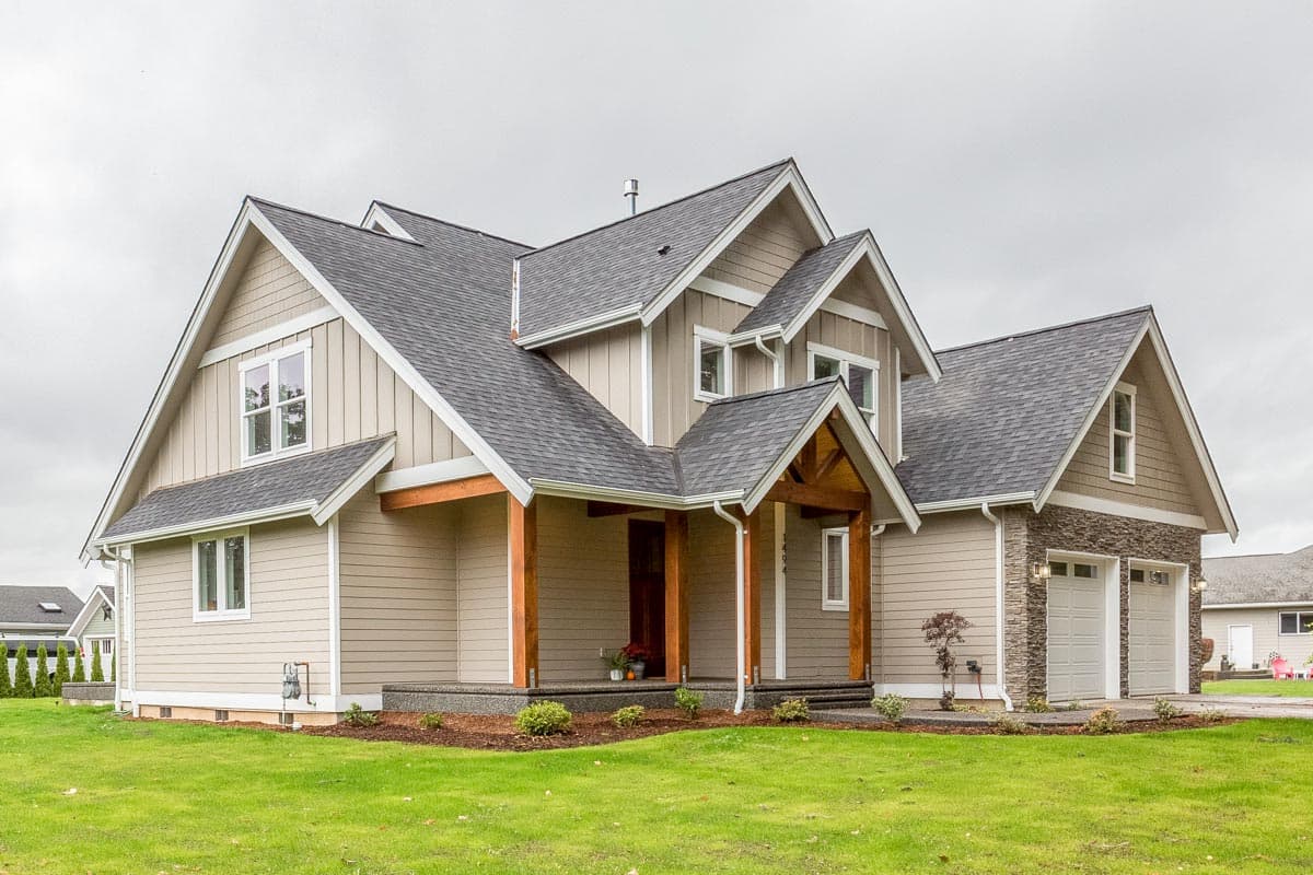 House plan exterior showcasing a two-story Modern Farmhouse with a covered porch, gables, dormers, and a stone-accented three-car garage.