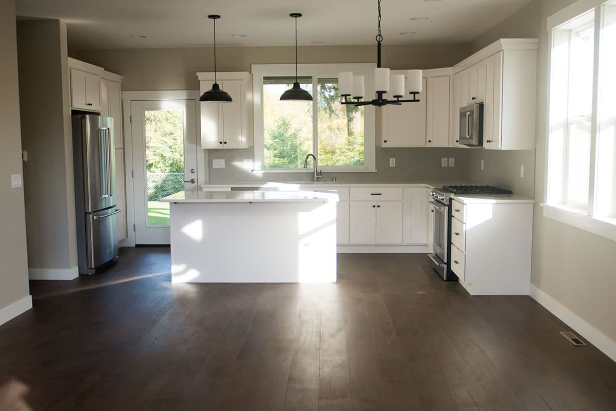 Kitchen interior with white cabinetry, central island, stainless steel refrigerator, and gas range. Natural light fills the space.