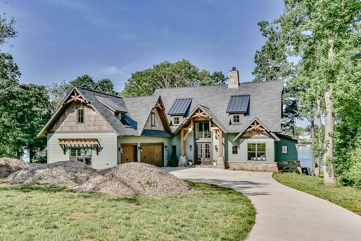 Craftsman style house plan exterior with a two-car garage, stone chimney, and prominent gables with timber accents.