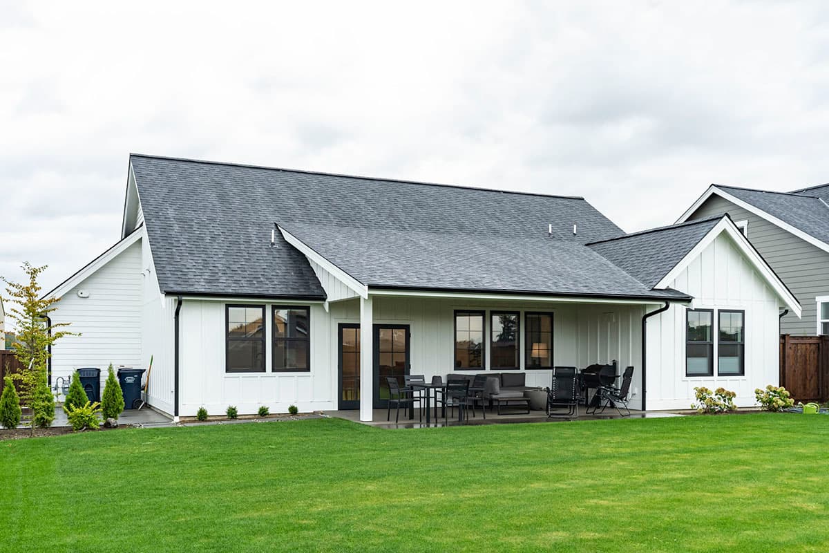 Modern Farmhouse house plan exterior with white board and batten siding, dark-trimmed windows, and covered patio.