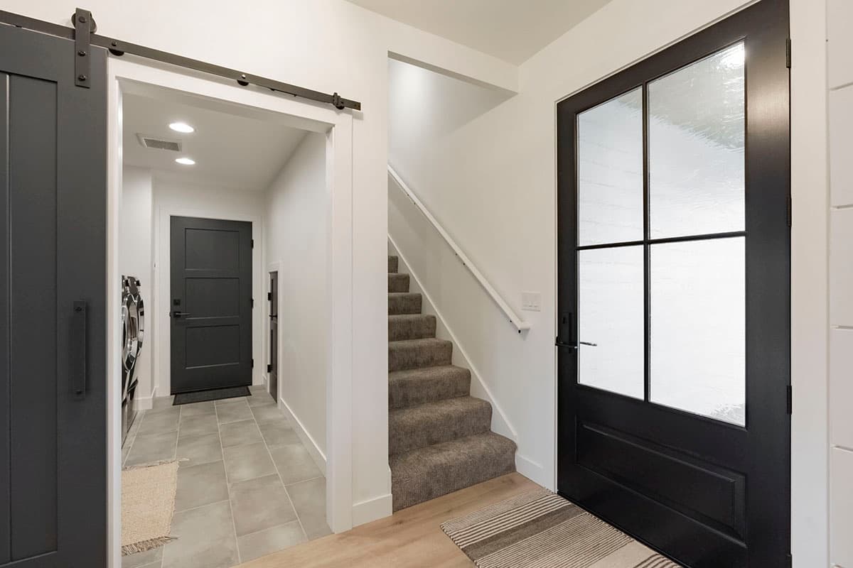 Interior view of entry with black front door, barn door, stairs, and laundry room access.