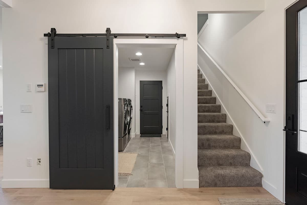 Interior view showing a laundry room with stacked washer/dryer, a sliding barn door, and a carpeted staircase.