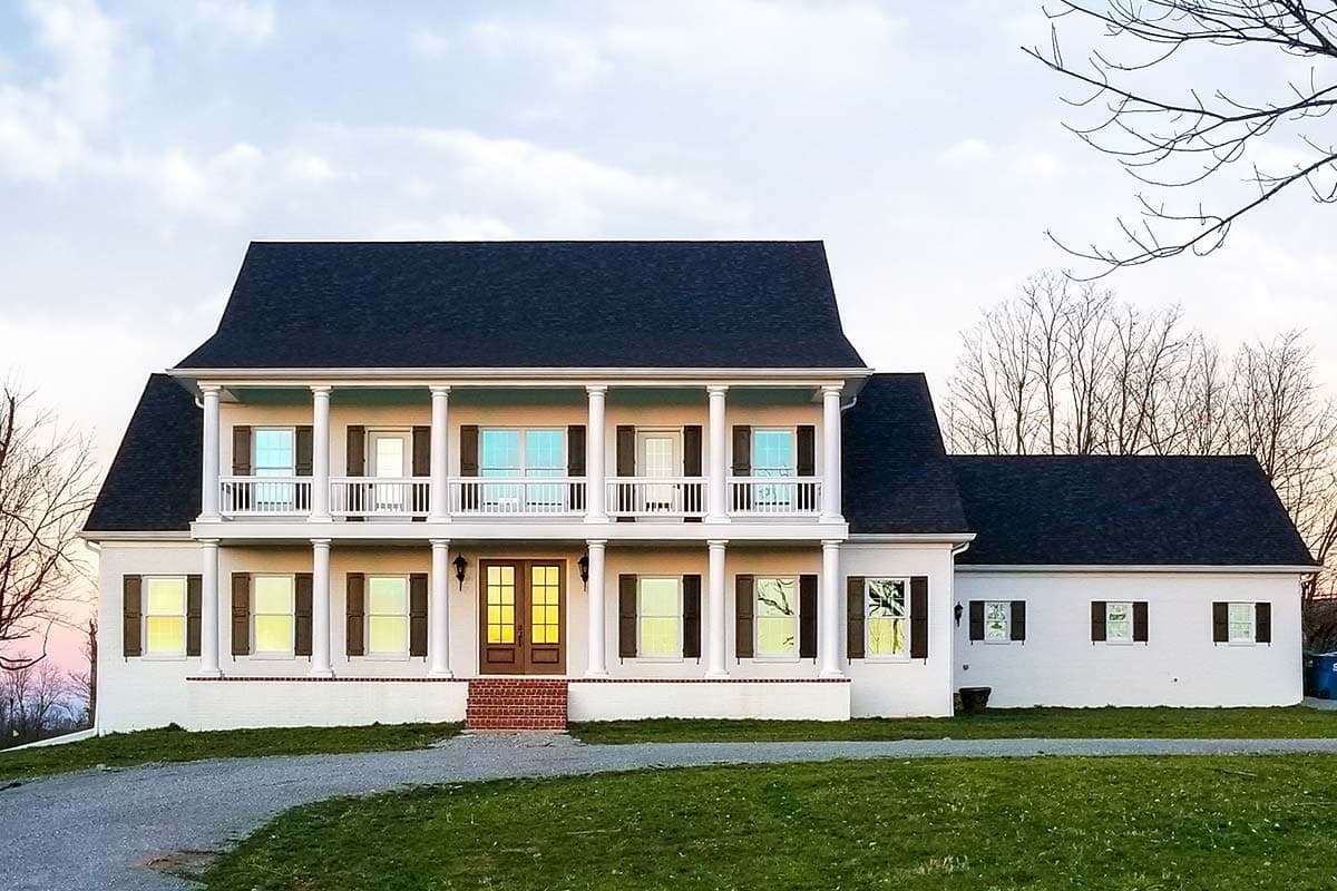House plan exterior. Two-story Colonial with a covered porch supported by columns. Features include shutters, a gabled roof, and a symmetrical facade.