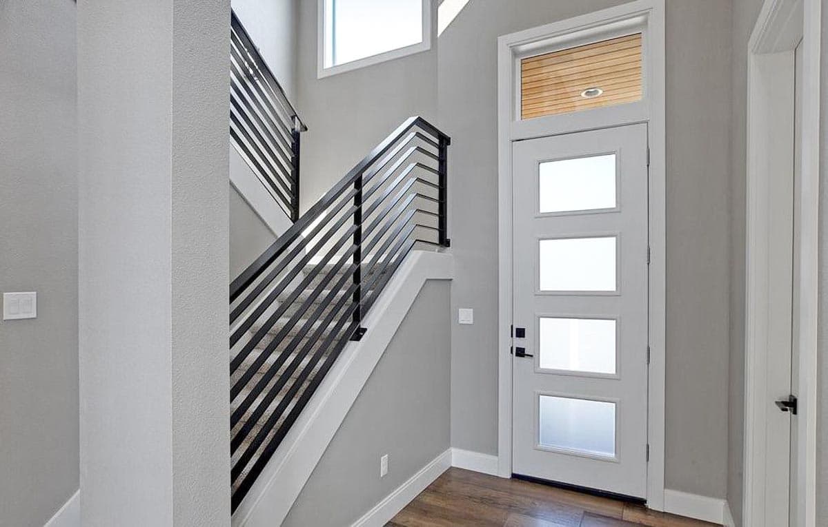 Modern entryway with a contemporary door featuring frosted glass panels and a staircase with black horizontal railings.
