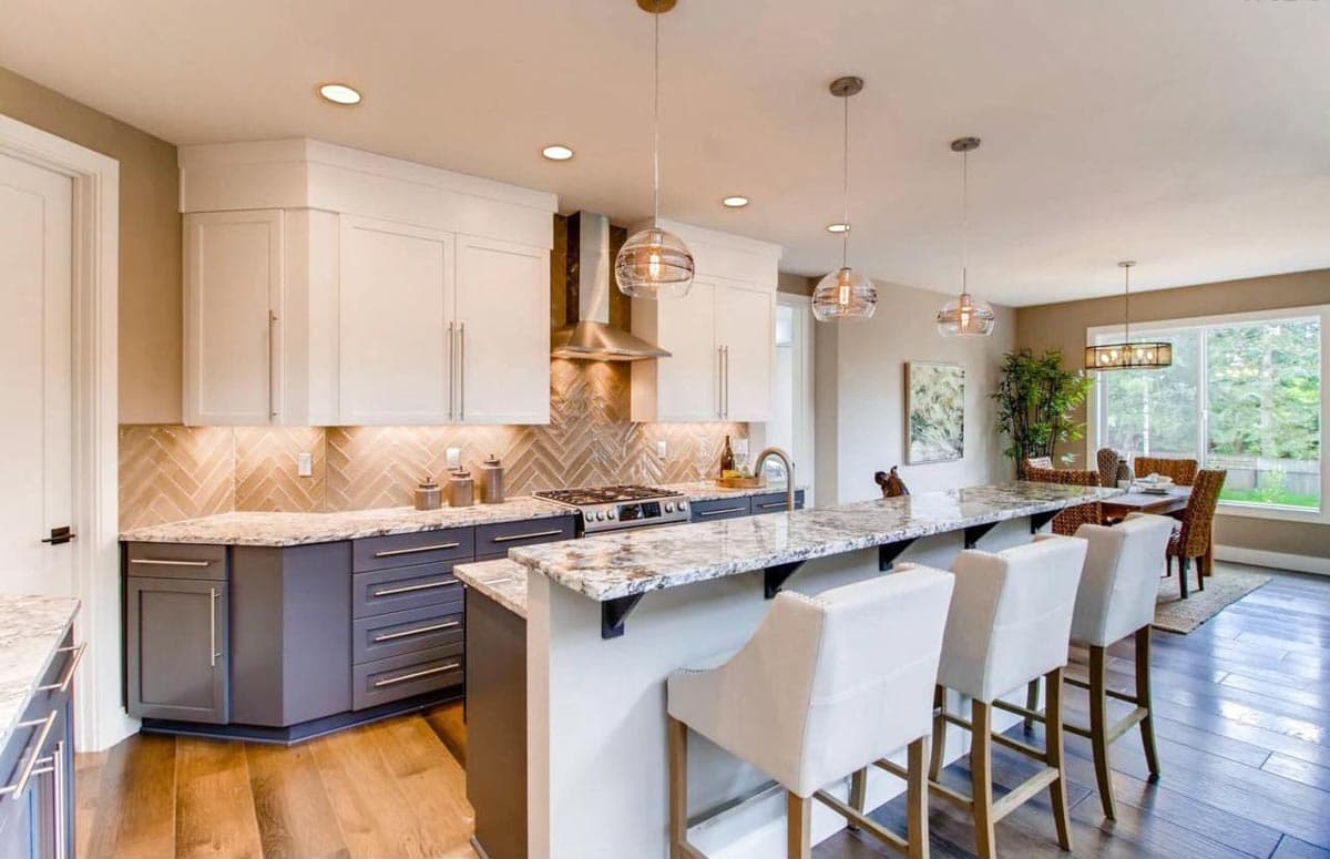 Kitchen featuring a large island with seating, white upper cabinets, dark lower cabinets, stainless steel appliances, and herringbone tile backsplash.