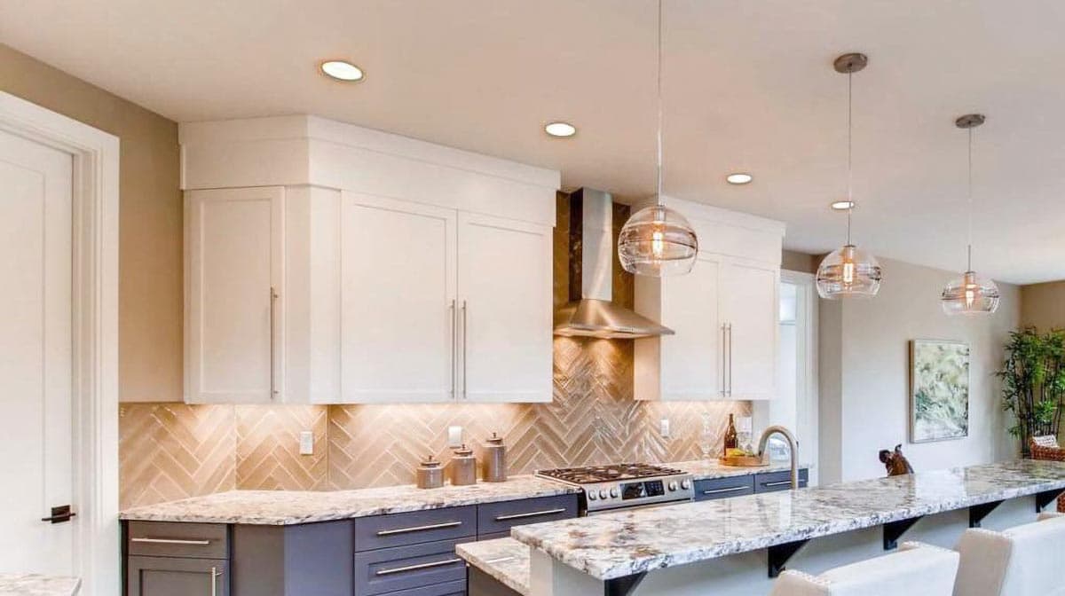 Kitchen with white upper cabinets, grey lower cabinets, granite countertops, herringbone backsplash, and pendant lighting.