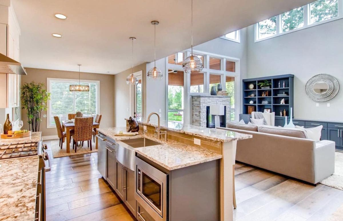 Open concept living space with kitchen island, dining area, and great room with vaulted ceiling and fireplace.