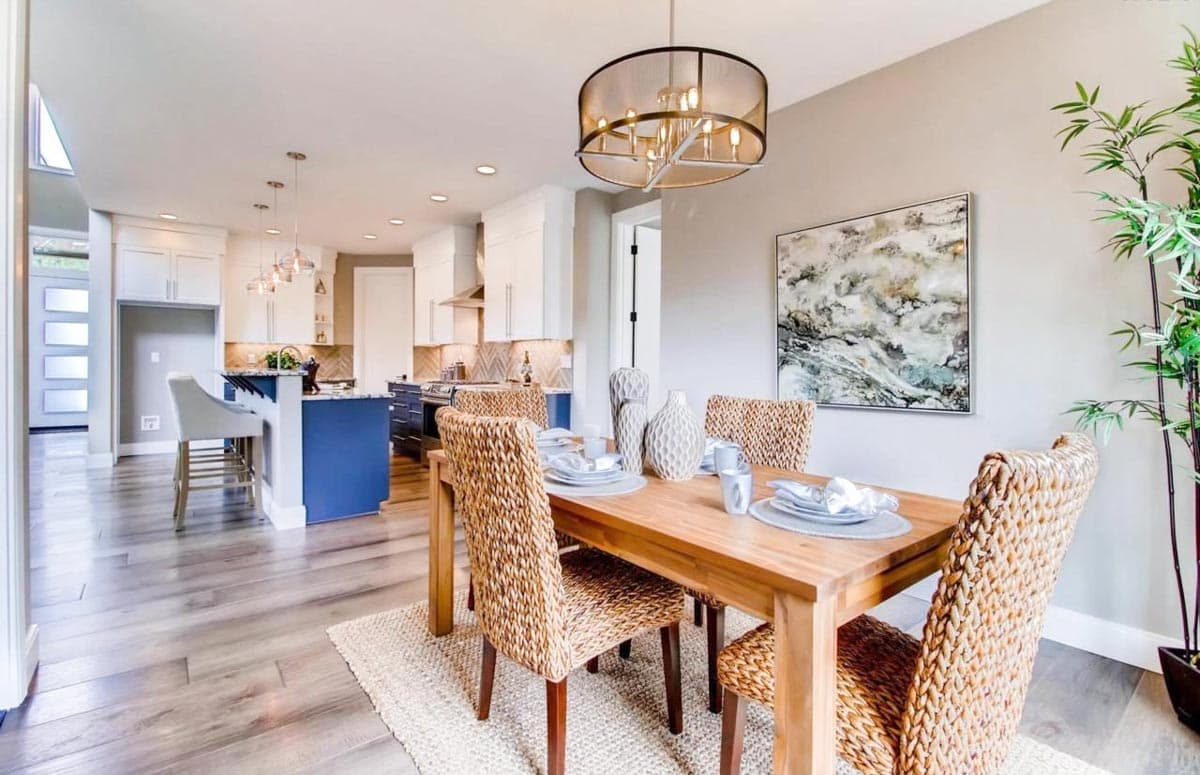 Dining area with chairs and table opens to kitchen with island, white cabinetry, and stainless steel appliances.