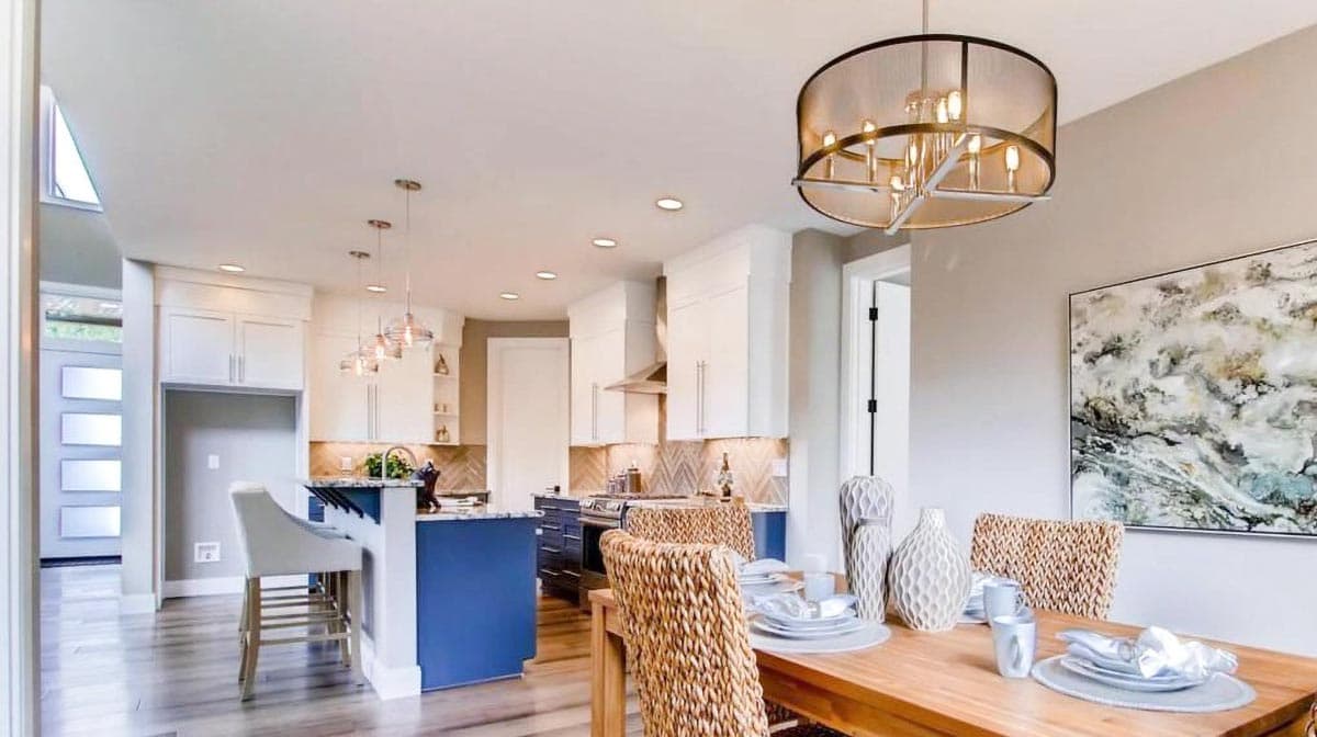 Open concept dining area and kitchen with blue island, white cabinetry, stainless steel appliances, and pendant lighting.