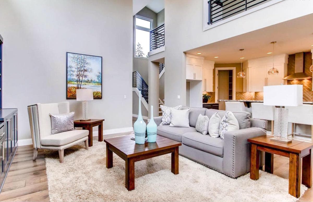 Interior view of an open-concept living area with a two-story staircase, adjacent kitchen, and vaulted ceiling.