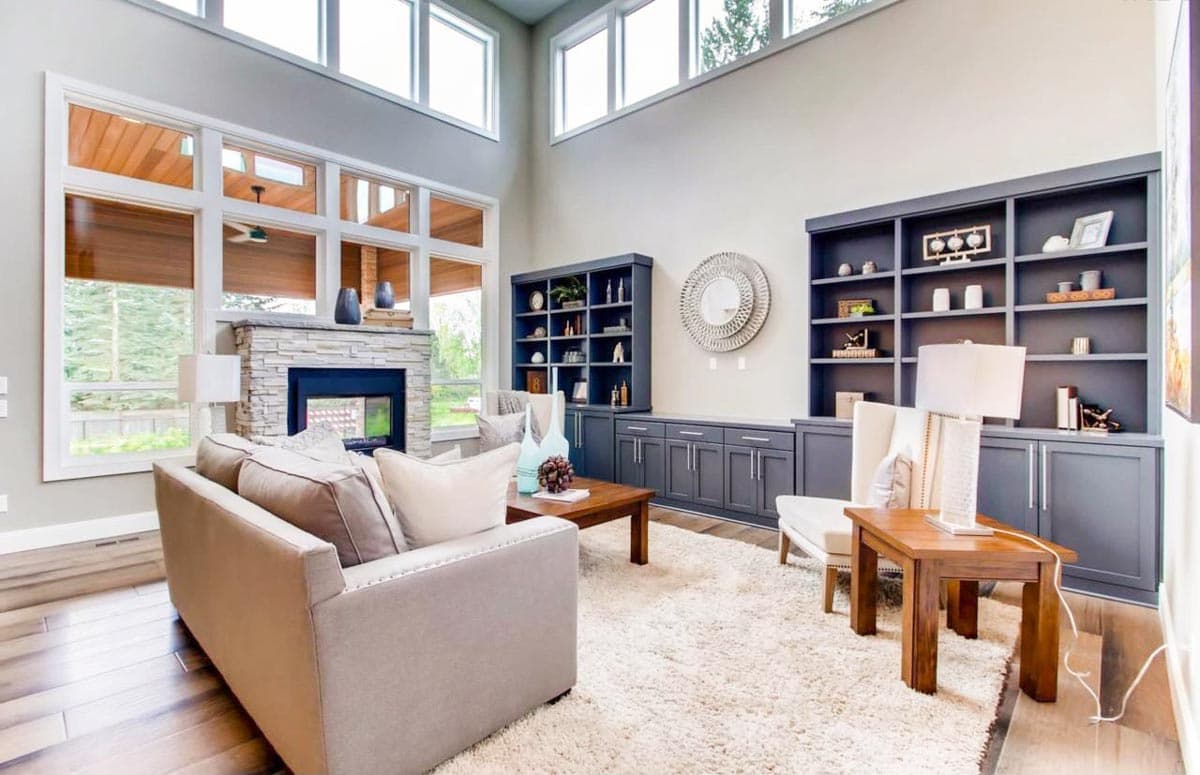 Living room with stone fireplace, floor-to-ceiling windows, built-in bookshelves, and high ceilings.