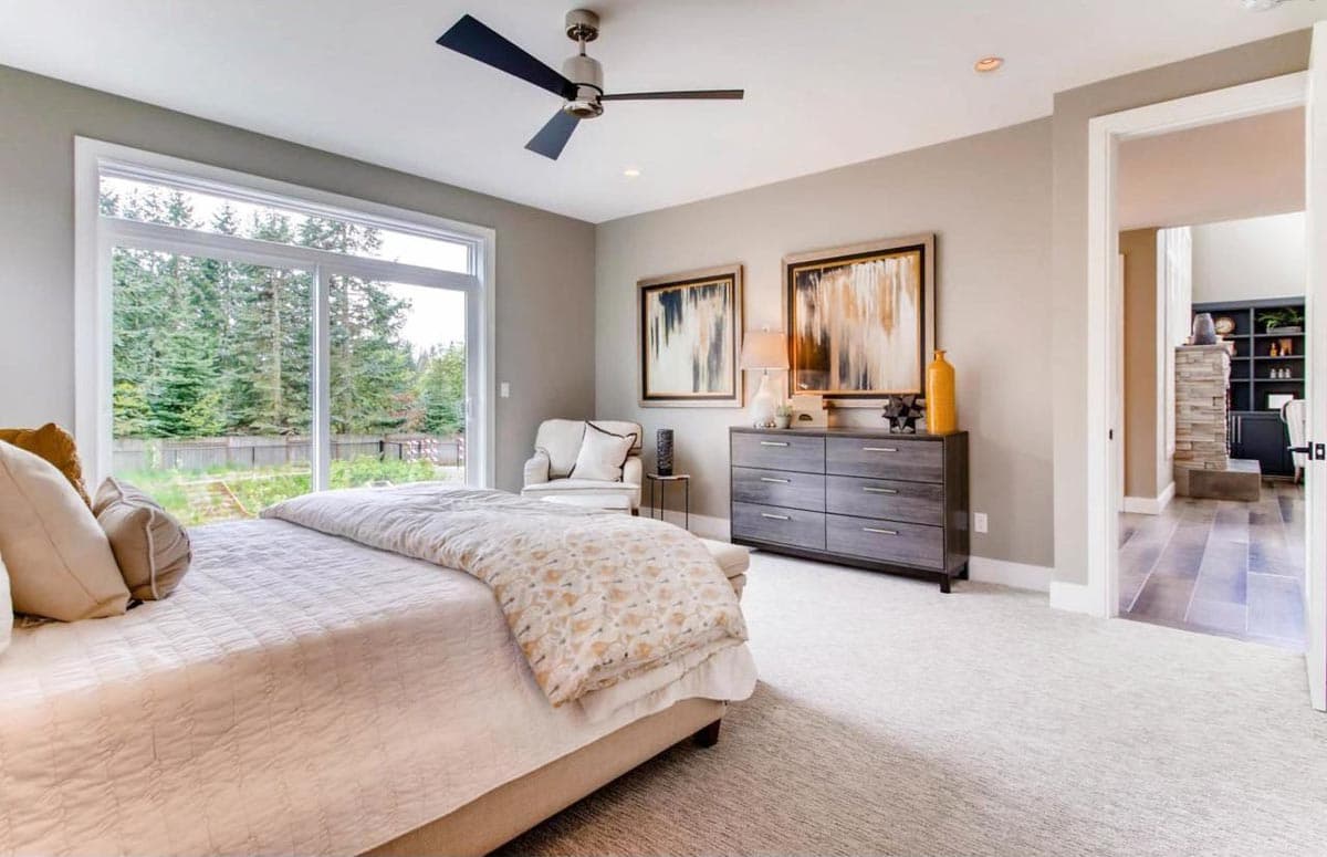 Primary bedroom with sliding glass door, ceiling fan, dresser, and an open doorway to a living area with a stone fireplace.