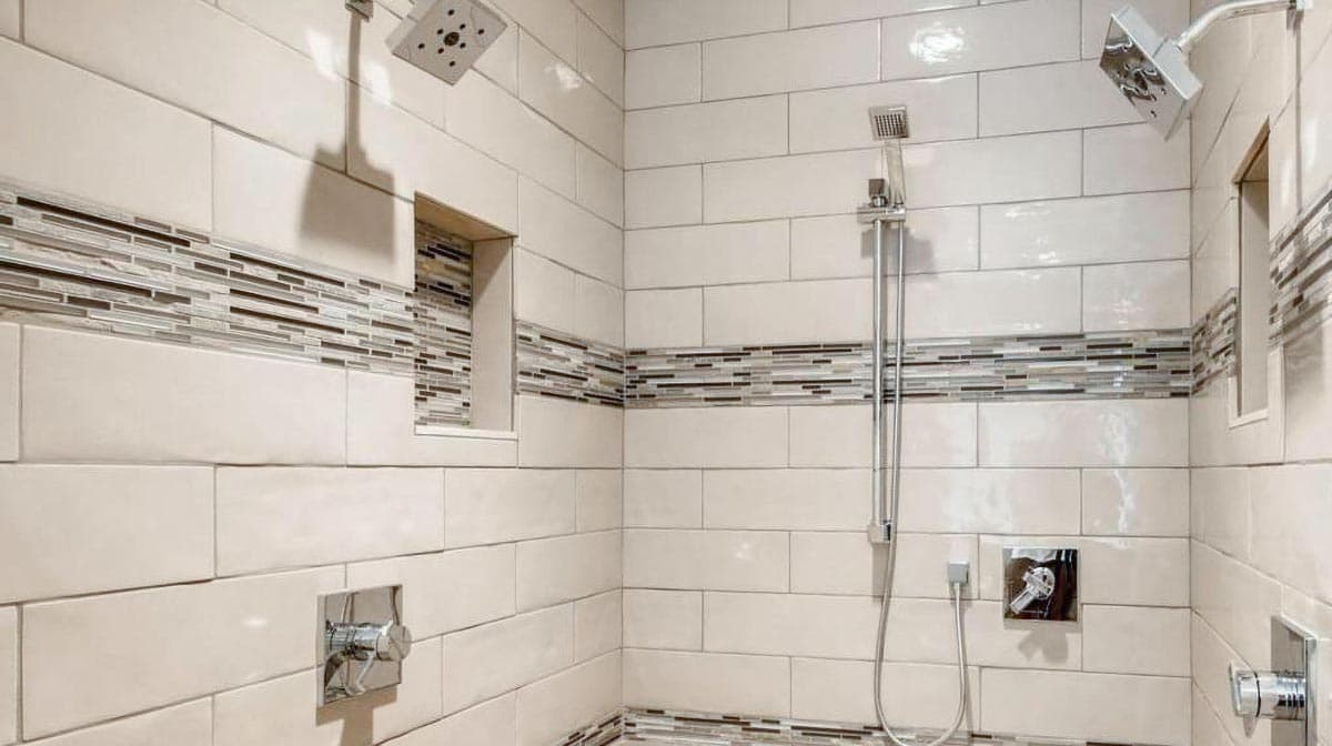 Modern shower with white subway tile, mosaic tile accent band, built-in niches, and dual shower heads.