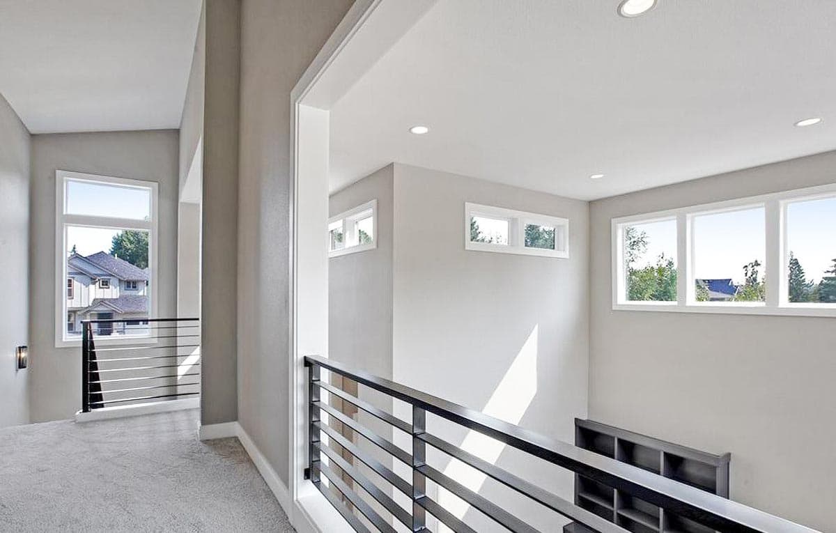 Interior hallway with a carpeted floor, modern horizontal railings, and multiple windows showcasing an exterior view.